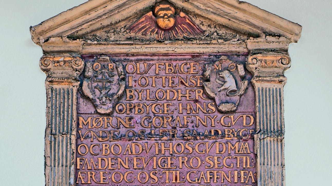 På tavlen står der: "Oluf Bager i Odense by lod her opbygge hans mødrene gård af ny. Gud onde os her så at bygge og bo at vi hos Gud må få den evige ro, sig til ære og os til gavn i faders, søns og Helligånds navn 1586".