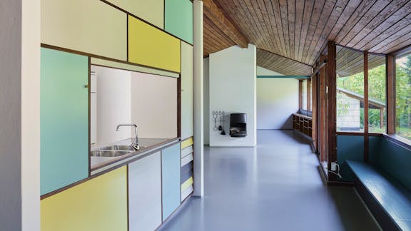 De farvede felter i køkkenet er skabe og skuffer, som kan åbnes fra begge sider, hvilket var praktisk, når der skulle dækkes bord og vaskes op.