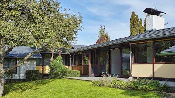 Skorstenen er husets eneste element i mursten. Facadens transparente udtryk får næsten skorstenen til at fremstå som en skulptur, huset er bygget op omkring.