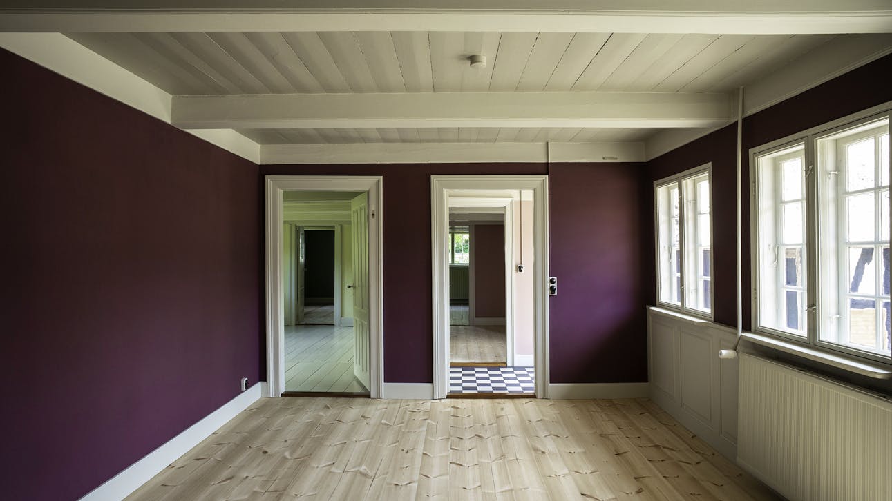Lyst rum med lyst trægulv, vægge i lilla og hvidt træloft med kig ind til andre rum.