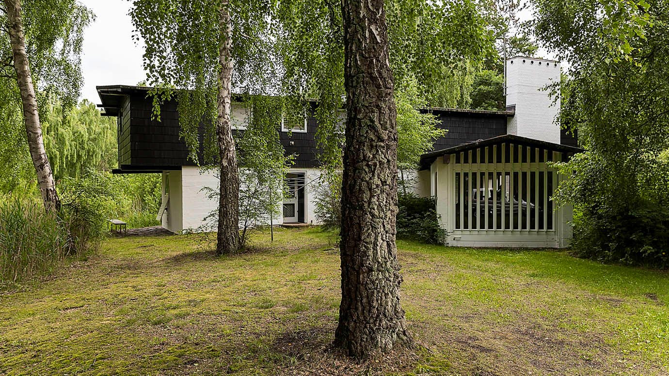 Husets facade med garagen til højre. Huset er omgivet af mange høje birketræer.