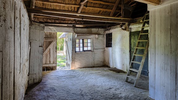 Stald i Stines hus med lerstampet gulv, hvidkalkede vægge og adgang til høloft via stige.