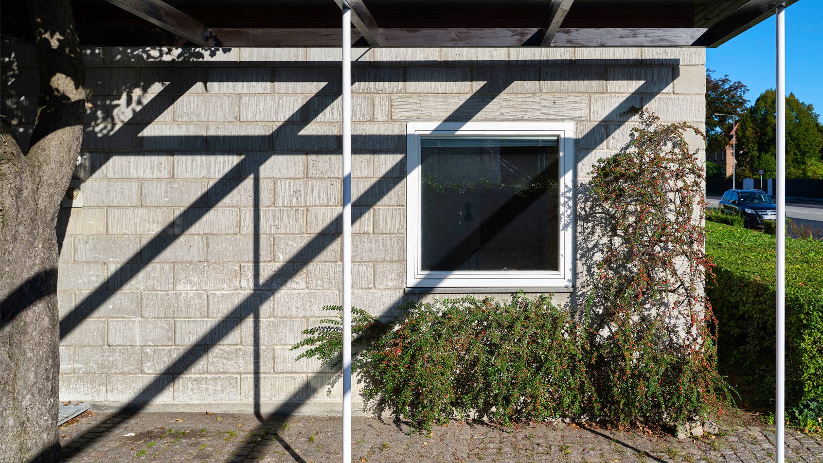 Forgård ved hoveddøren i Vilhelm Lauritzens eget hus – præcist murværk i betonblokke, skyggevirkninger fra pergola og slyngplanter som blød kontrast.