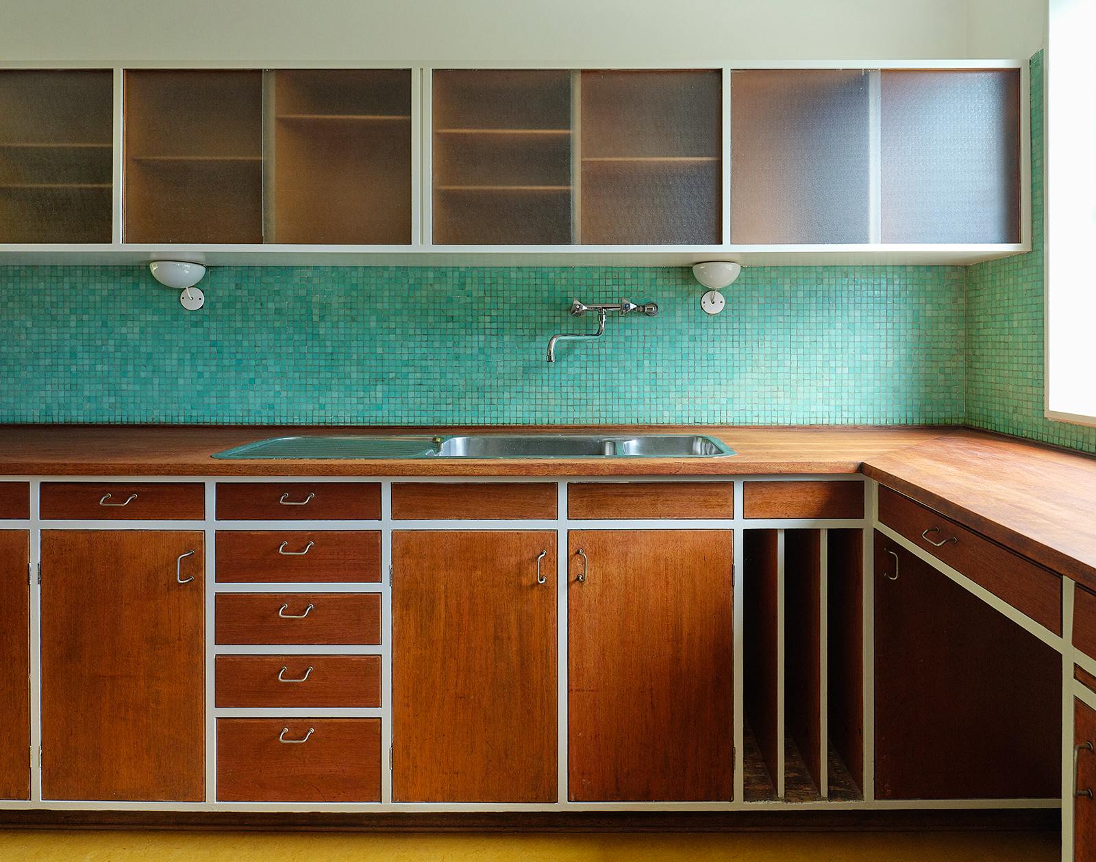 Køkken i Vilhelm Lauritzens eget hus med grøn mosaikvæg, varme træfronter og overskabe med matteret glas.