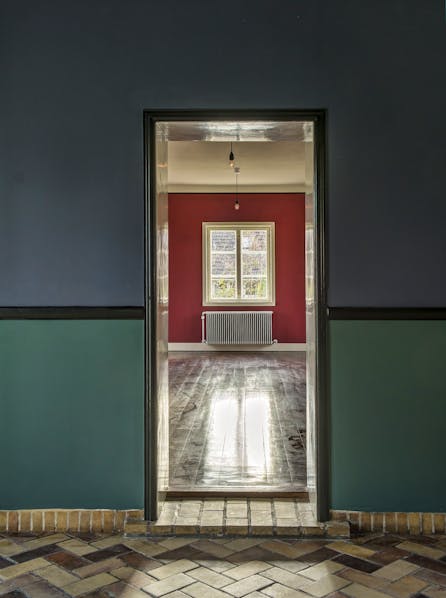 Kig fra den runde spisestue ind mod stuen, hvor de dybe farver og materialeskift understreger rummenes karakter.