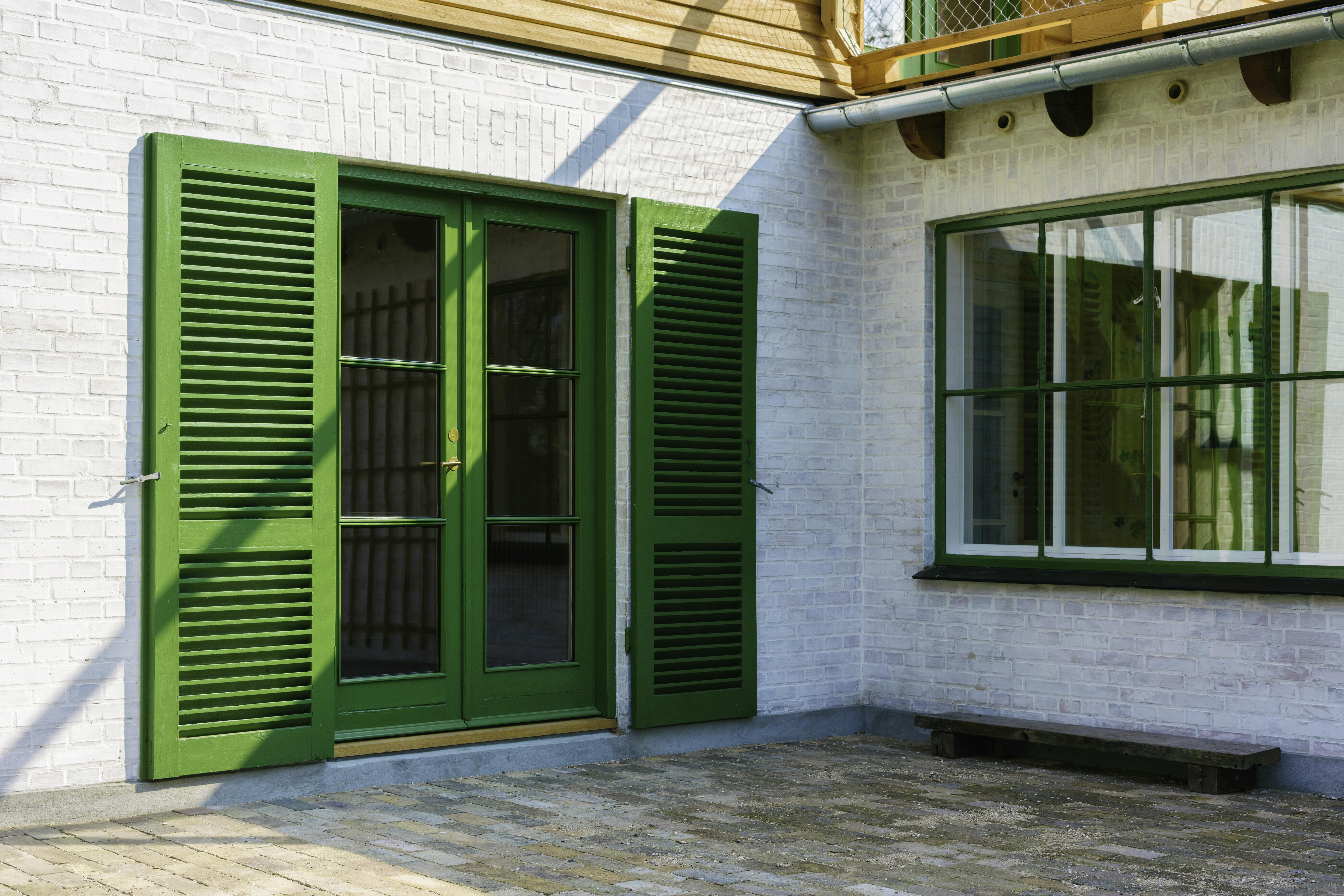 Terrassedør med grønne skodder og sprosset glas i Viggo Møller-Jensens eget hus, flankeret af hvidmalet murværk og vindue med grøn ramme.