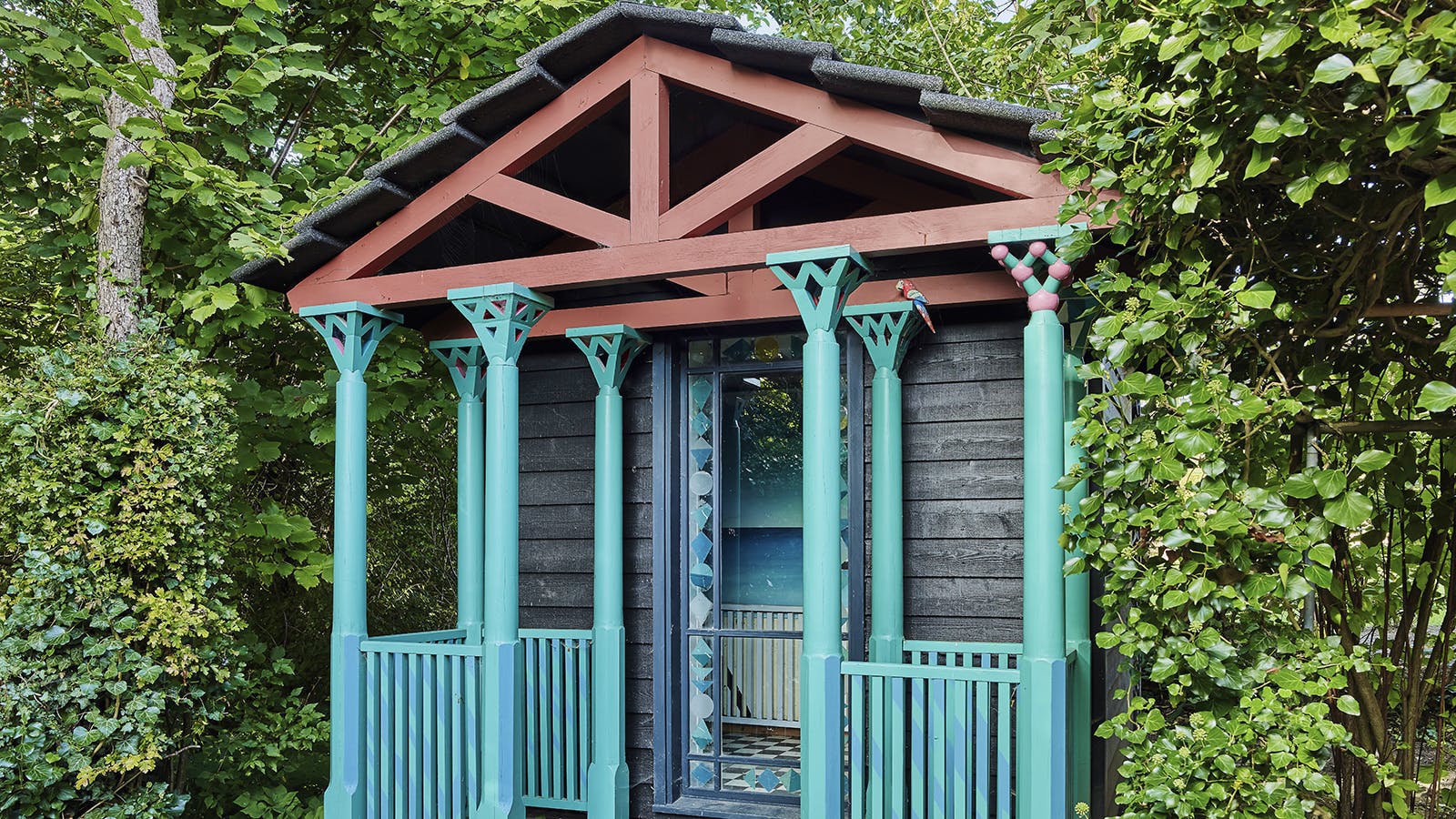 I haven står et yndefuldt lille  hus, et farverigt lille lysthus,  hvis konstruktion arkitektparret har moret sig med  at forme både konstruktivt  og skulpturelt. Alt sammen i  festlige farver.