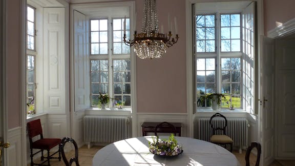 Rosa stue på Hindsgavl Slot med udsigt til park og sø.