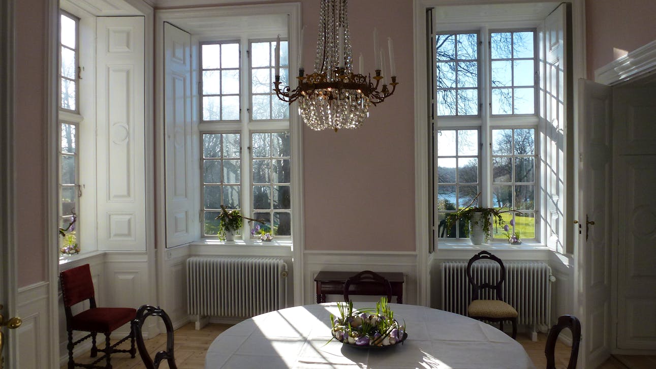 Rosa stue på Hindsgavl Slot med udsigt til park og sø.