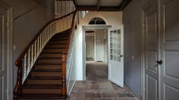 Hallen med åbent trapperum og klassicistisk kvartsvingstrappe i mørkt træ og lyse balustre.