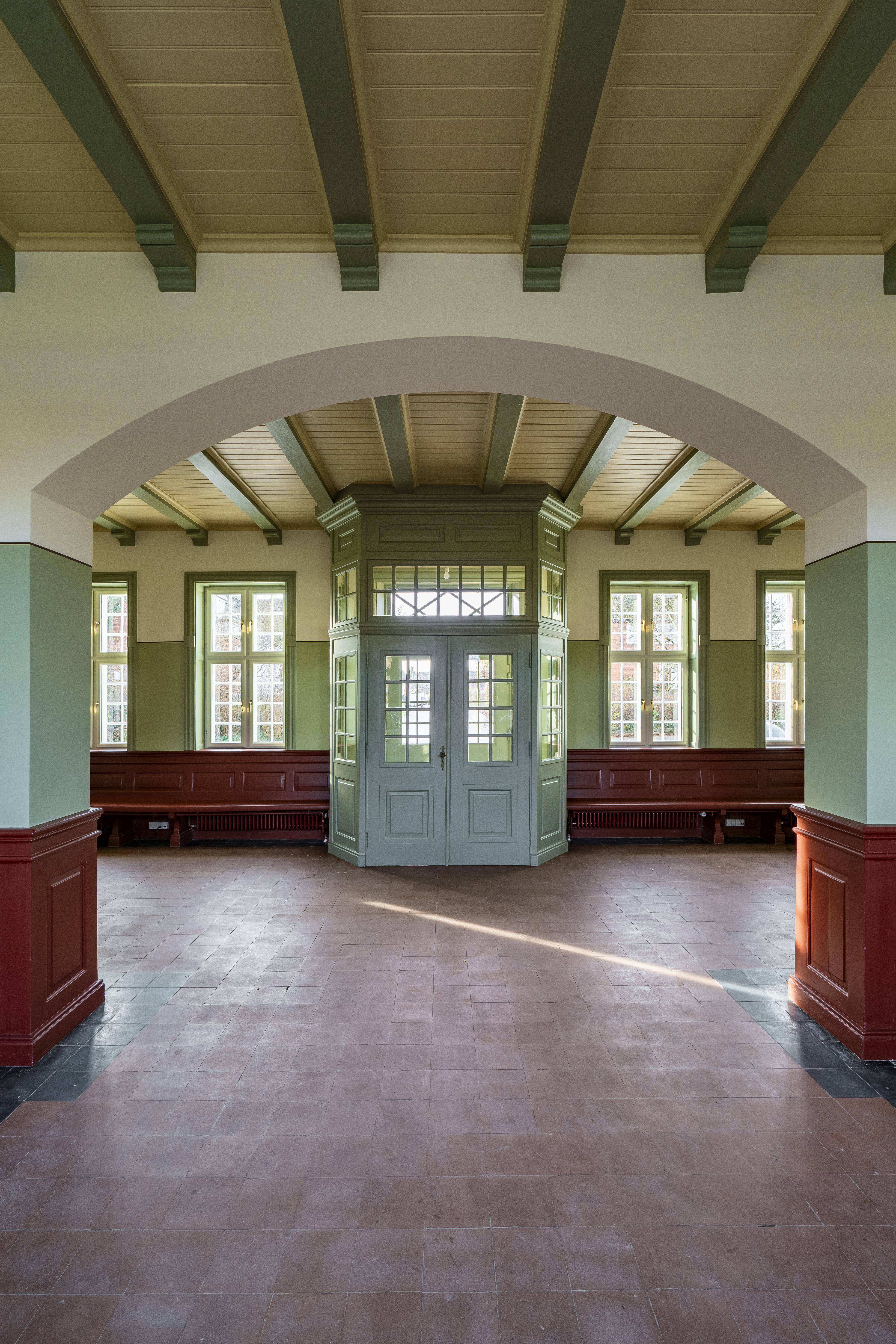 Det grønne vindfang er placeret i midten af ventesalen, omgivet af røde bænke og lysegrønne vinduesrammer.