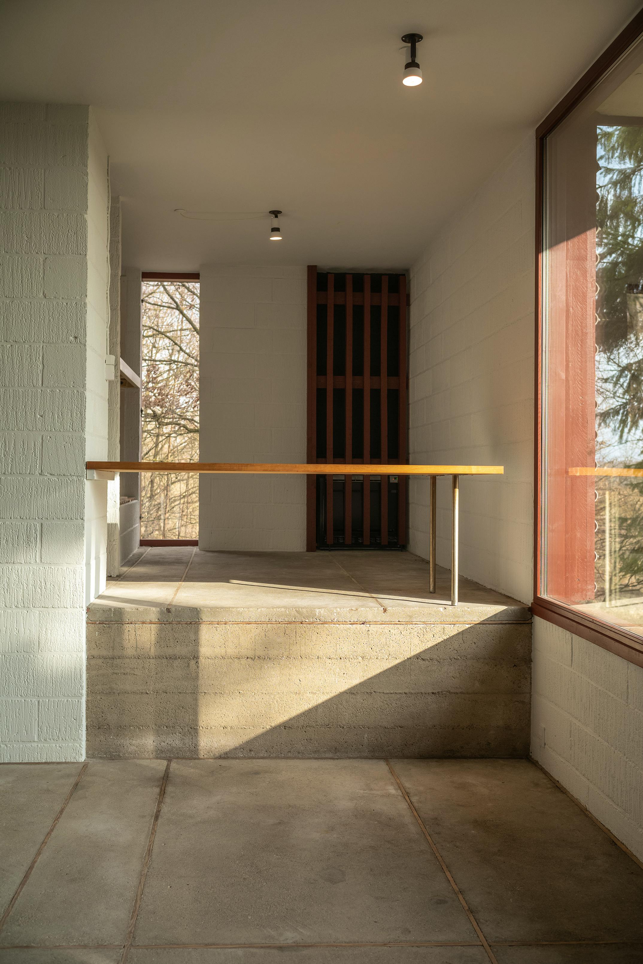 Skrivebord i Poul Erik Thyrrings eget hus placeret ved stort hjørnevindue, med lav halvmur af in-situstøbt beton og vægge af gasbeton strøget med kalk.