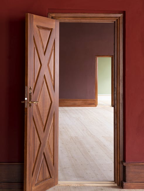 Kig gennem åbne døre til rum malet i rødlige og brunlige nuancer i Søetatens Pigeskole.