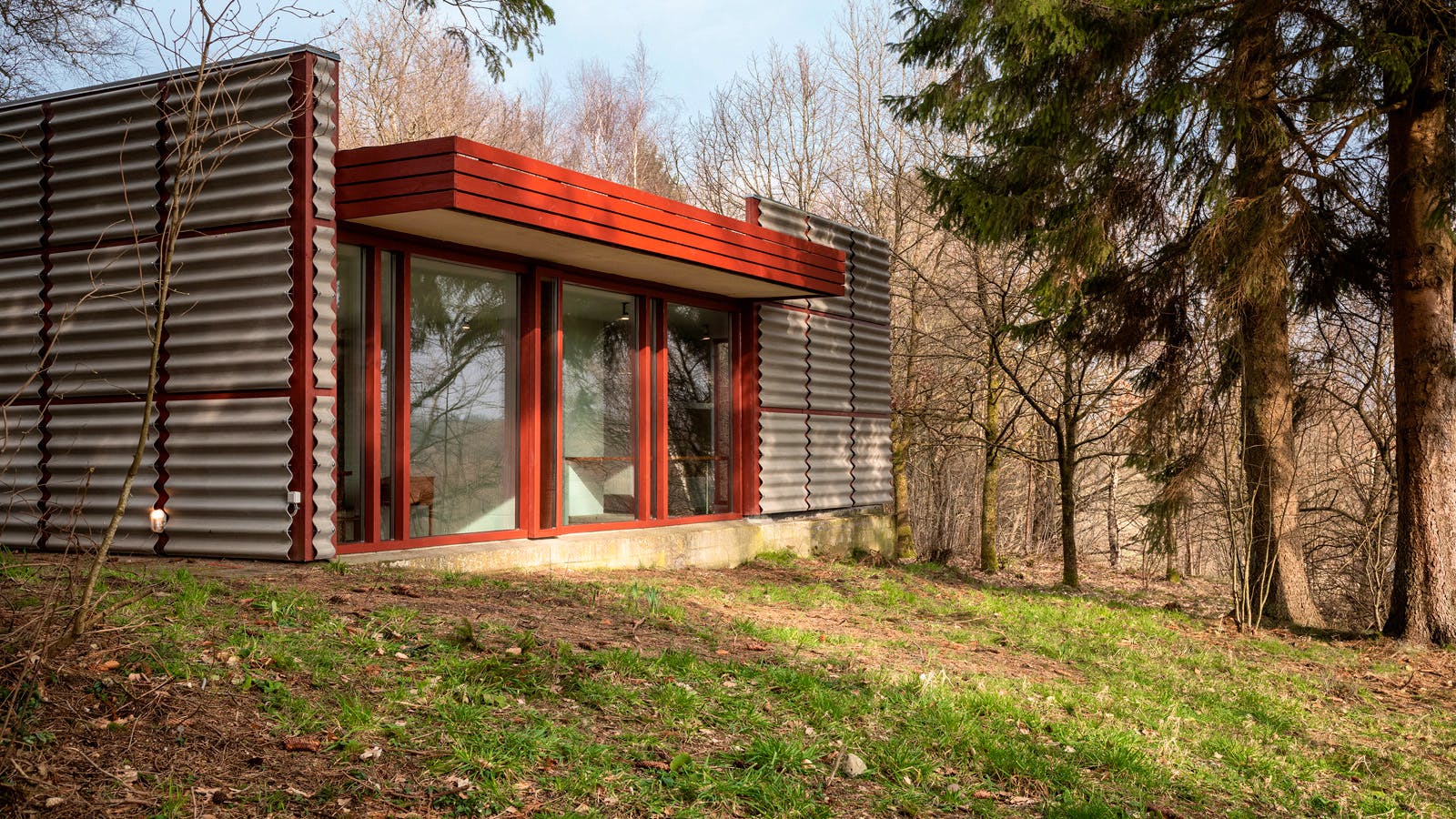 Panoramavindue i Poul Erik Thyrrings eget hus med bølgende facade og røde rammer, i kontrast til den omkringliggende skovnatur.