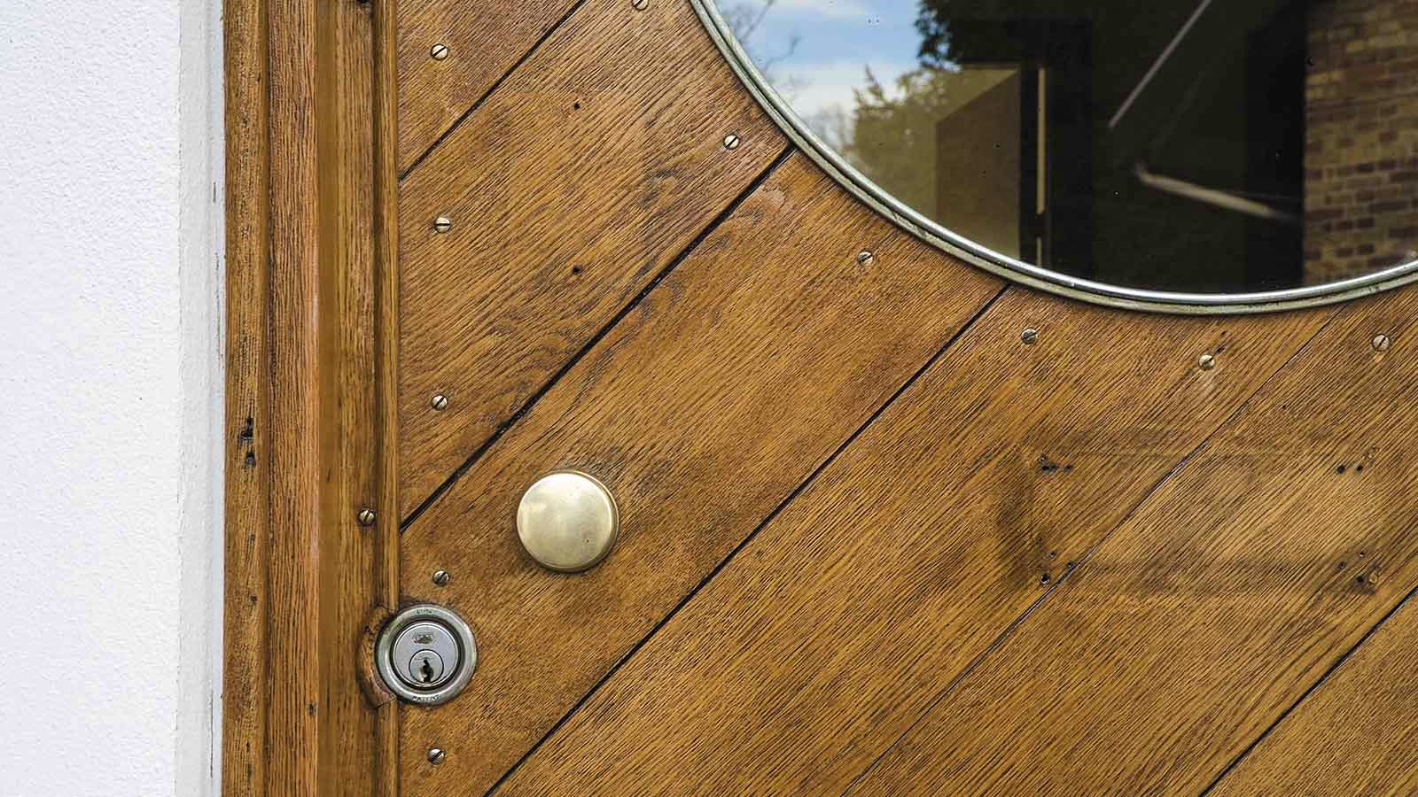Detalje af hoveddøren med maritimt koøje i toppen, messingfarvet dørhåndtag og cylinderlås.