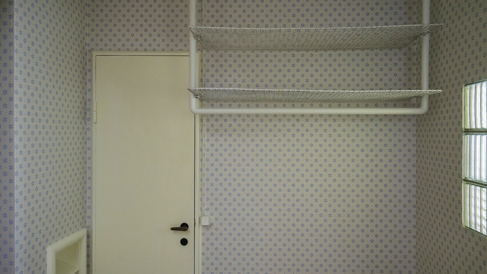 Entré med det genskabte tapet “Blå Kornblomst” og originalt garderobemøbel i net og rør.
