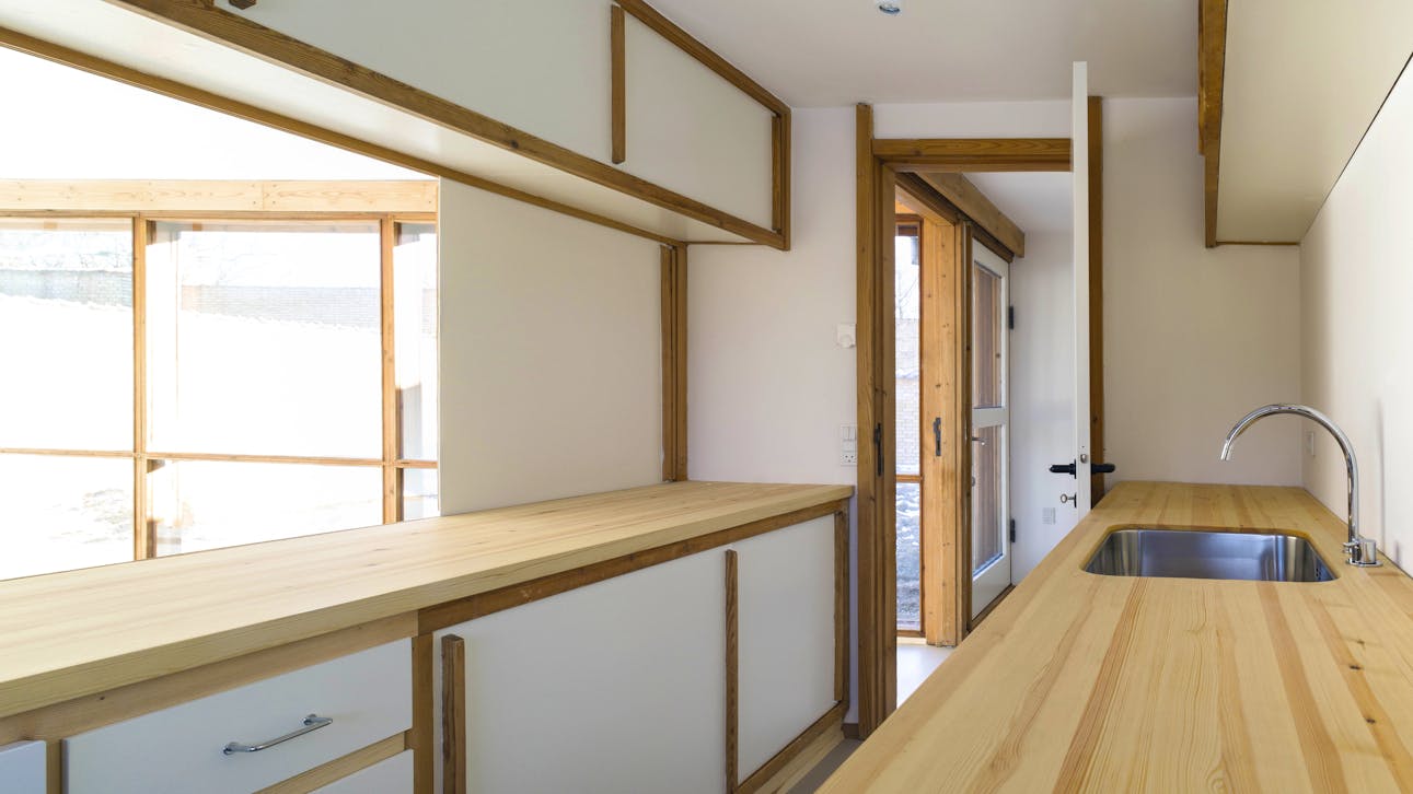 Køkken i Romerhuset med lyse træoverflader og enkle, indbyggede skabe.