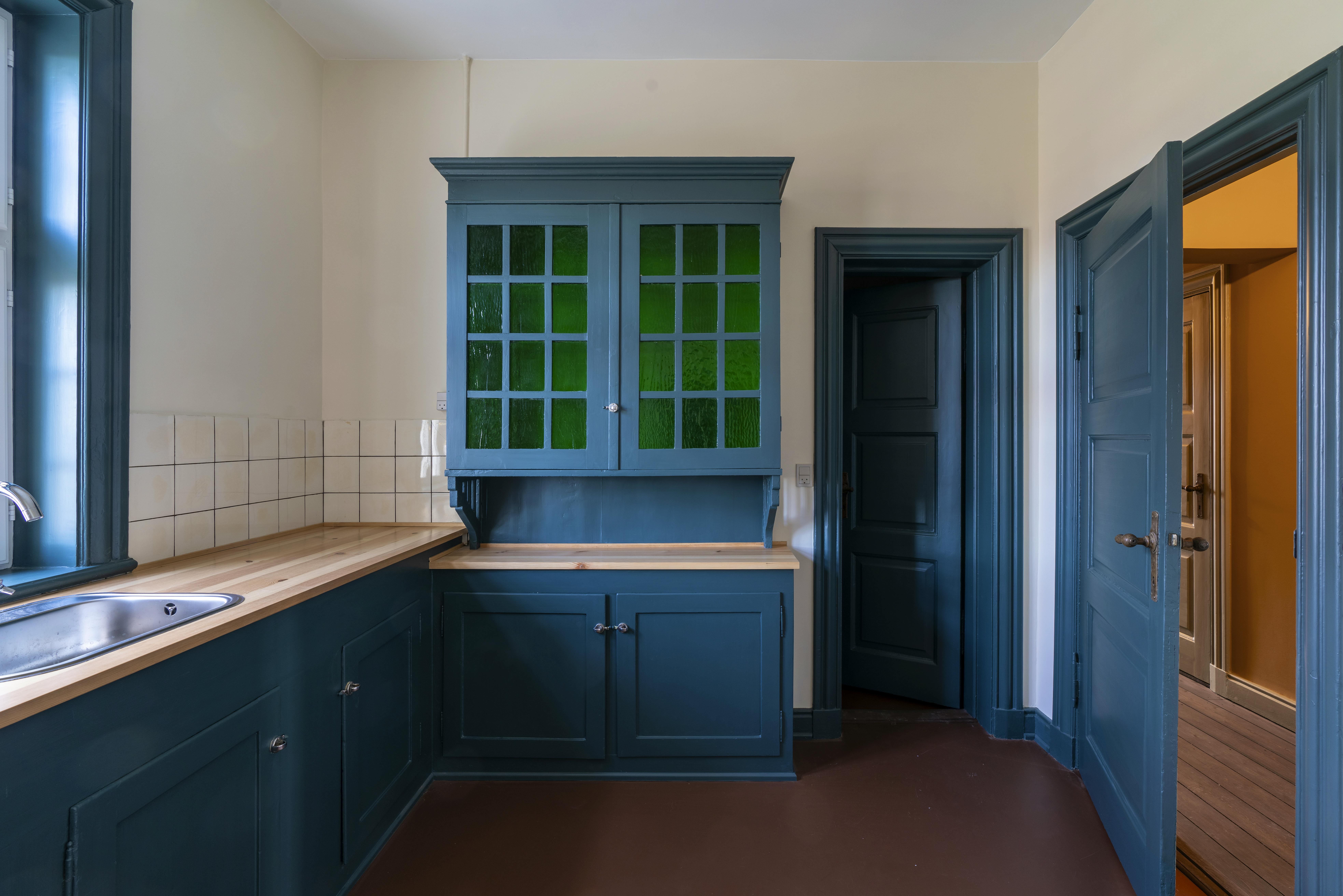 Det originale køkken i stationsforstanderens lejlighed er restaureret med mørkeblå skabslåger og grønt glas i overskabet.