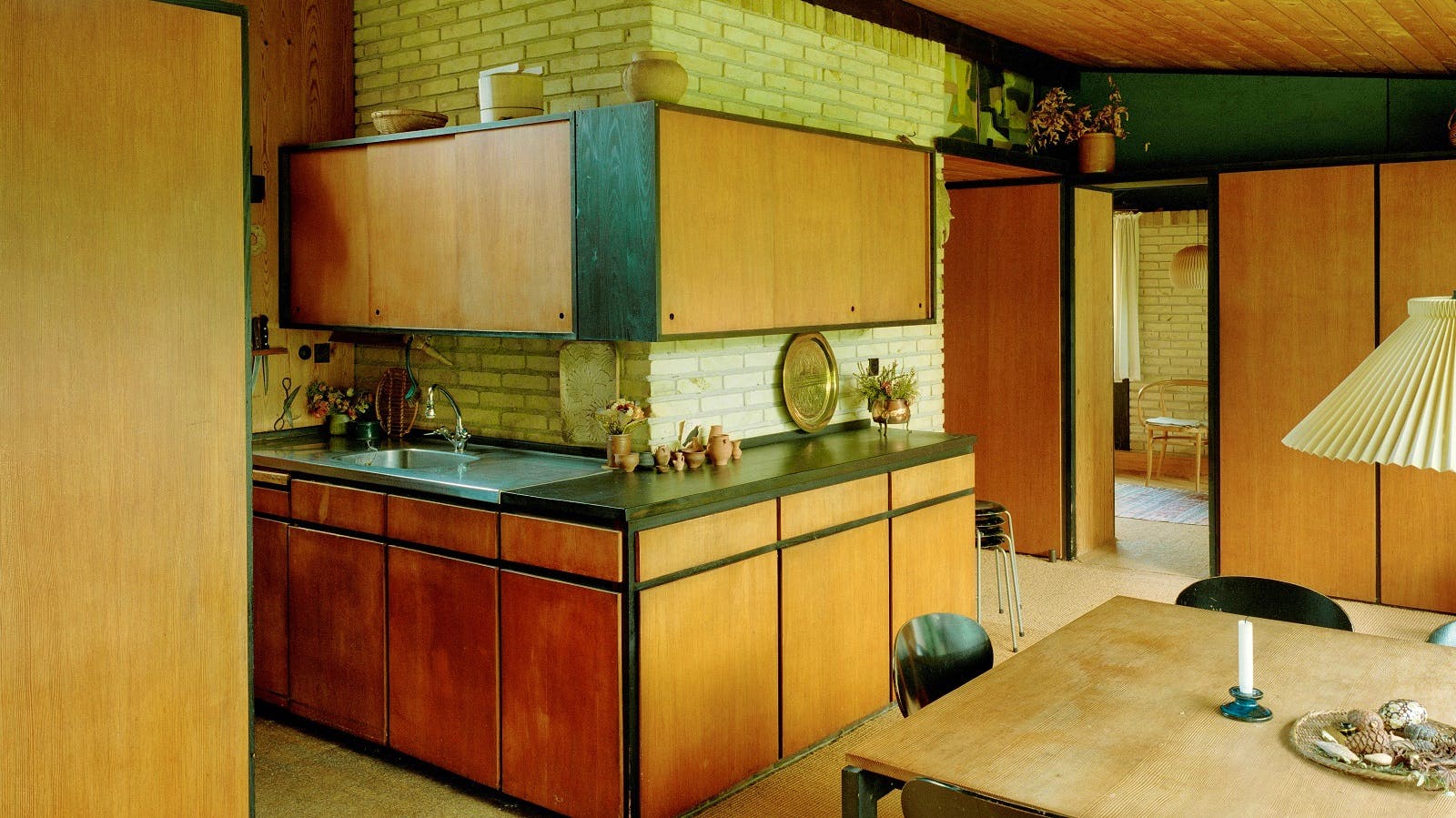 Køkkenet i Bertel Udsens hus er med med lyse træskabe, sort bordplade og stålvask.