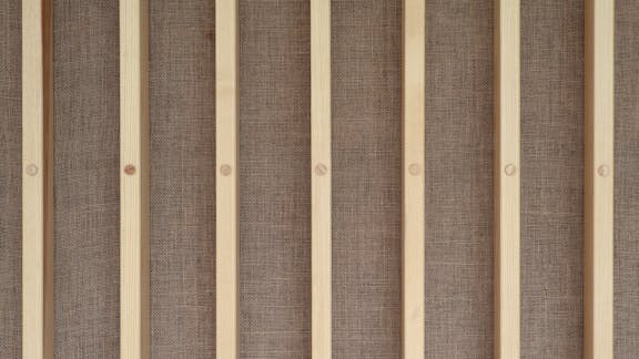 Detalje af vægbeklædning i Glasalstrup – lodrette trælister monteret på baggrund af hessian.