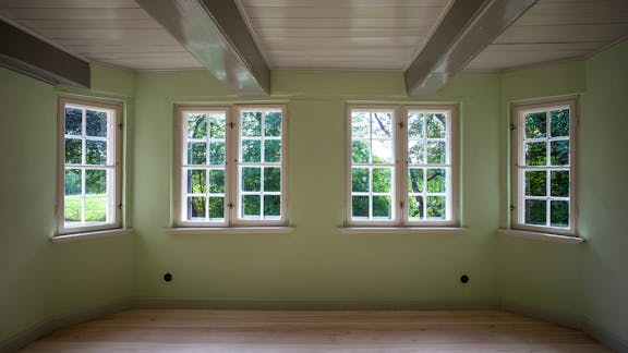 Lys grøn stue på Nørre Sødam med karnap, fire vinduer, lyse trægulve og synlige loftbjælker.