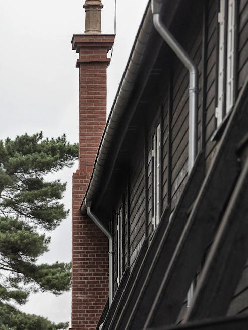 Murstensskårsten på sidehuset med den sortbeklædte træfacade set fra siden.