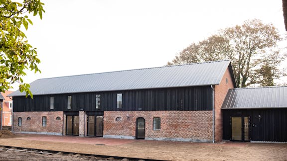 Laden ved Marskgården i Højer med teglstensmur og sort træbeklædning.