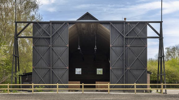 Fronten på ballonhangaren med de store sorte træporte åbne, set fra ridebanen.