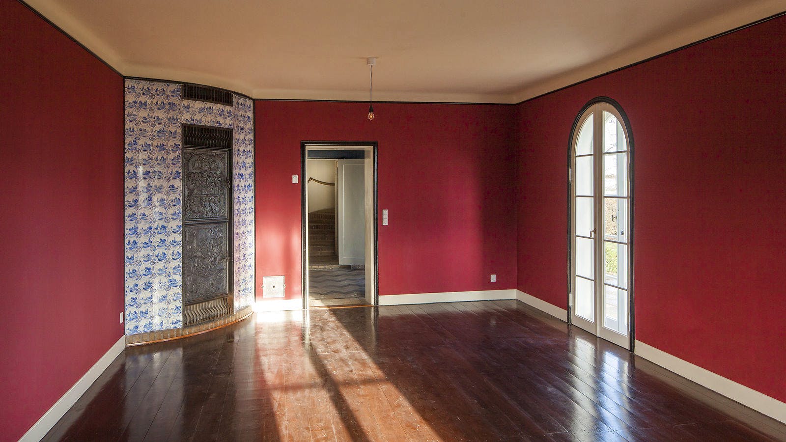 Husets dagligstue med bræddegulv, hvor der nu er installeret gulvvarme. Den gamle kakkelovn med de originale fliser og ovnlåger er bevaret som dekoration.