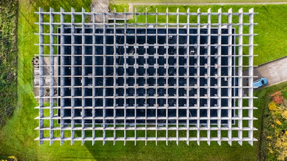 Luftfoto af Glasalstrup viser bygningens karakteristiske gitterstruktur i beton – et stramt, modulært net i grønne omgivelser.
