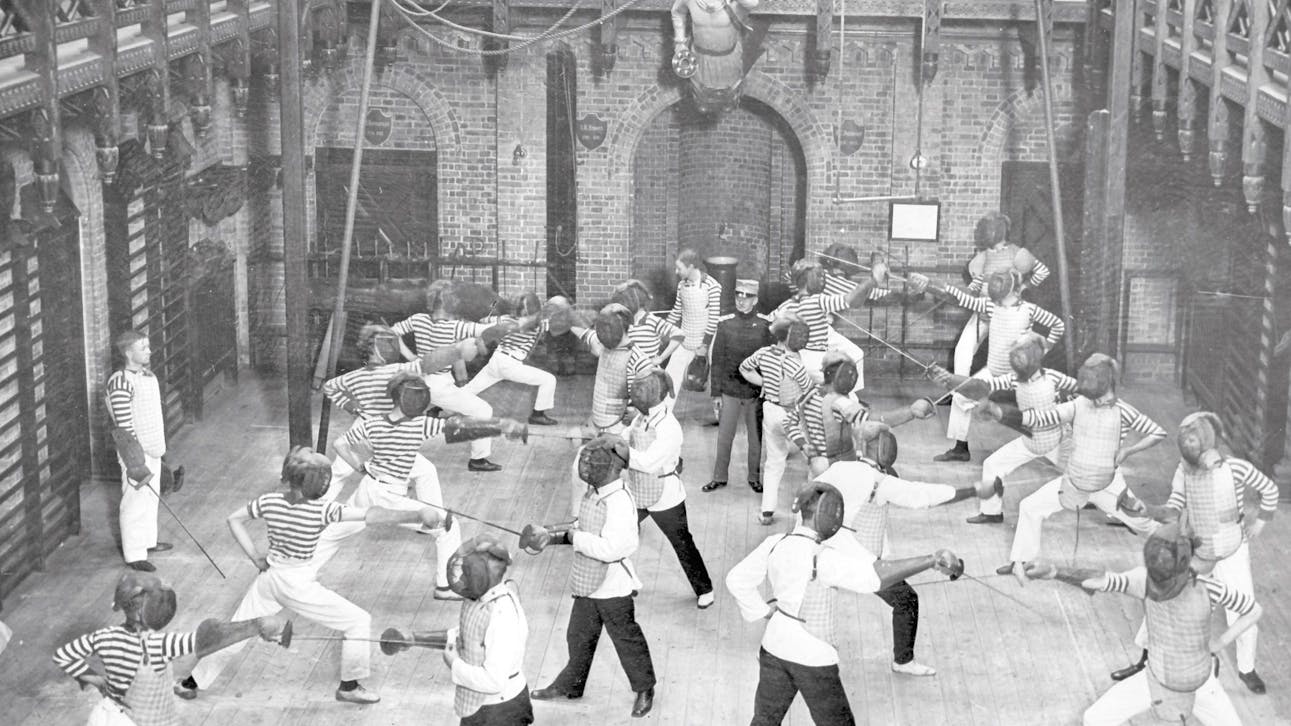 Historisk billede af skolebørn, der øver fægtning i den store sal.