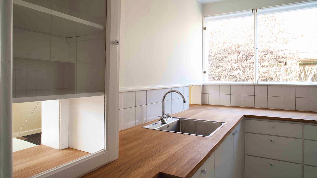 Køkkenet i Edvard Heibergs eget hus, med træbordplade, hvide låger og lem til spiseområdet.