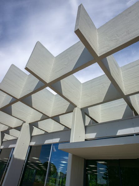 Facade med krydsformet betonkonstruktion og spejlende glaspartier under blå himmel.
