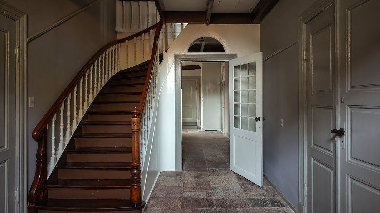 Hallen med åbent trapperum og klassicistisk kvartsvingstrappe i mørkt træ og lyse balustre.