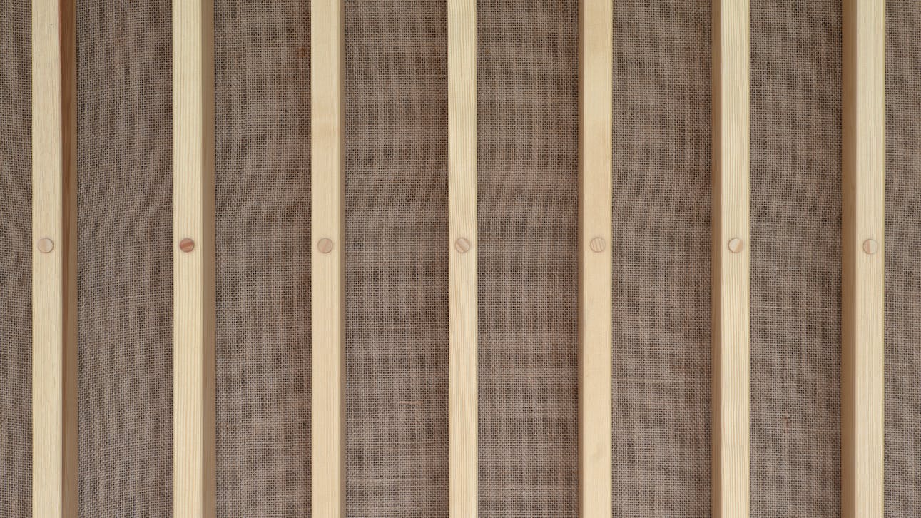 Detalje af vægbeklædning i Glasalstrup – lodrette trælister monteret på baggrund af hessian.