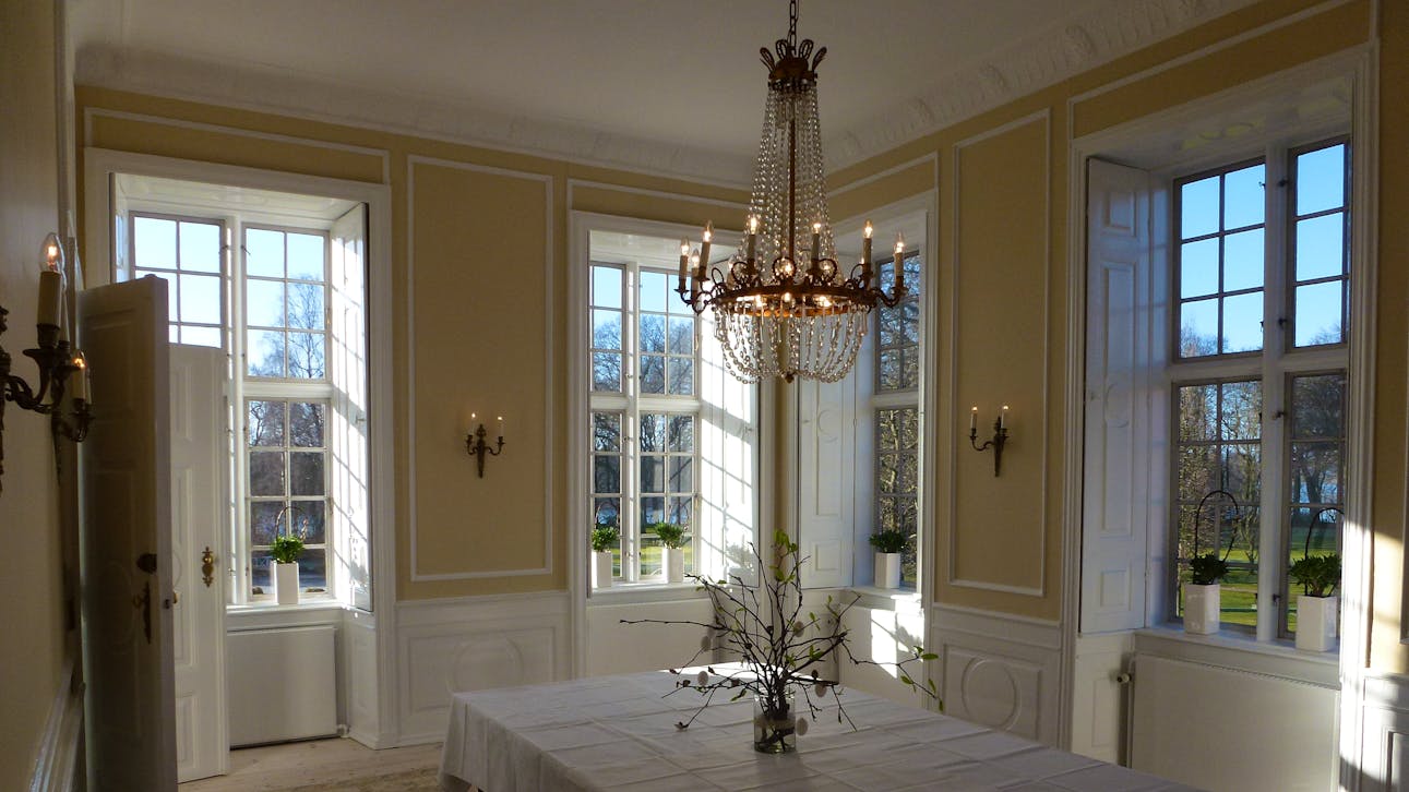 Lille spisestue på Hindsgavl Slot med lysegule vægge, store sprossevinduer og klassisk lysekrone.