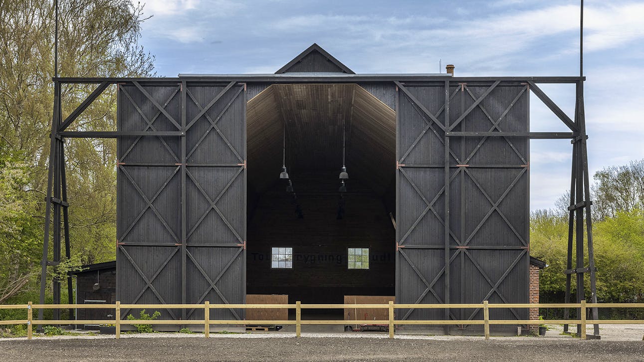 Fronten på ballonhangaren med de store sorte træporte åbne, set fra ridebanen.