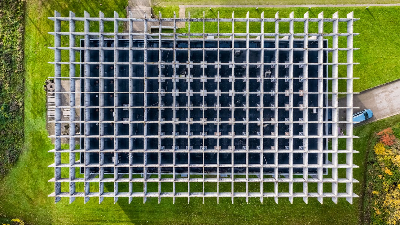 Luftfoto af Glasalstrup viser bygningens karakteristiske gitterstruktur i beton – et stramt, modulært net i grønne omgivelser.